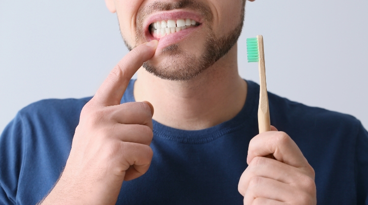 Man pointing to bleeding gums while holding toothbrush – Why Your Gums Bleed.